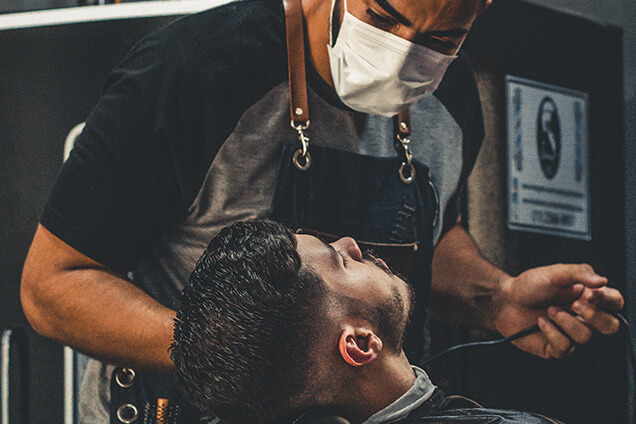 a barber with face mask on styling a beards of a man
