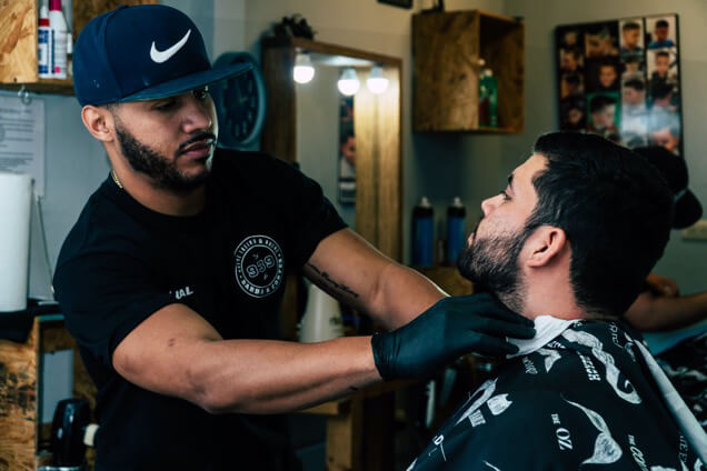 a barber in black cap and tshirt styling a man beards using trimmer
