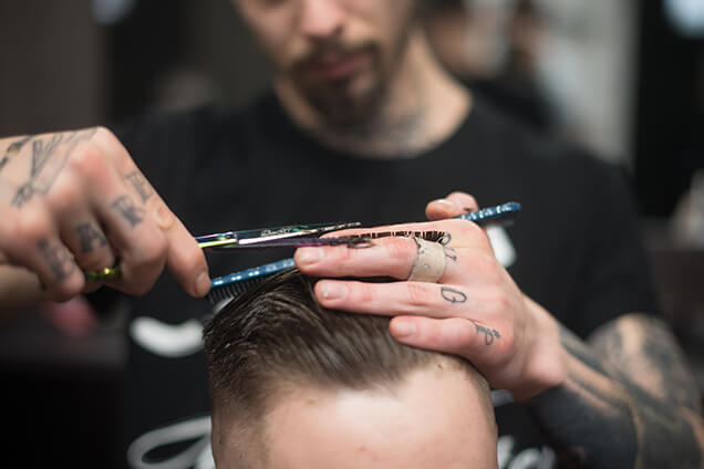 a barber is cutting hair of a man using scissor and comb